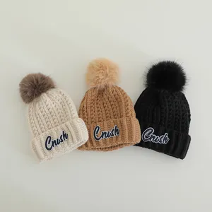 Detail of warm winter knit hats in cream, camel, and black with pom-poms and Crush patches
