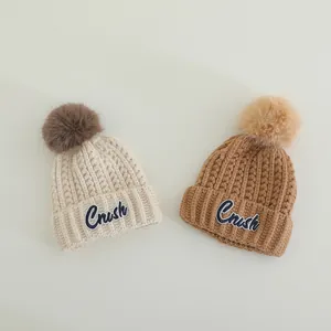 Detail of warm rib-knit beanies with fluffy pom-poms and embroidered Crush patches