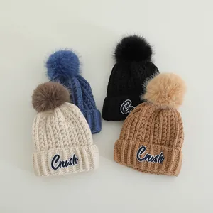 Close-up of ribbed knit beanies with fluffy faux fur pom-poms and Crush embroidery detail