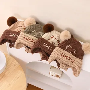 Close-up of four knitted bear earflap hats with pom-poms and LUCKY embroidery detail