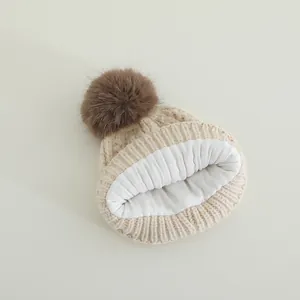 Close-up of the thick knitted off-white winter hat with a fluffy brown pom-pom and warm lining
