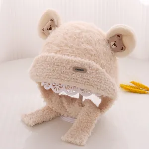 Detailed close-up of beige plush earflap hat with bear patch and fuzzy texture