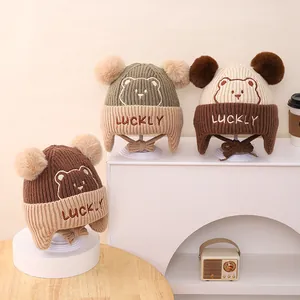 Detail of winter knit baby hats with pom-poms, Lucky bear embroidery, and ear flaps