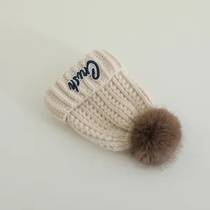 Detailed close-up of cream knit winter hat featuring pom-pom and Crush embroidery