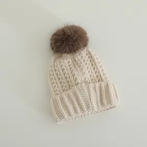 Detailed knit texture of children's warm beanie with a large fluffy brown pom-pom