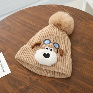 Detail van gebreide babymuts met pluizige pompon en puppy-borduurwerk op houten tafel