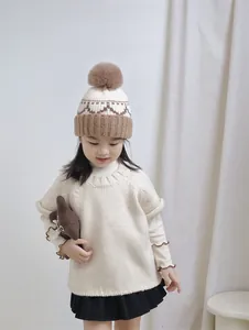 Close-up of beige knit hat with brown pompom and intricate diamond texture patterns