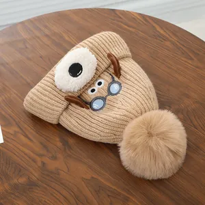 Detail van de gebreide babymuts met schattig puppy-cartoonontwerp en pluche bal in karamel