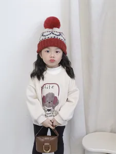 Detail of child wearing a red and white knit pom-pom hat with a dog graphic sweatshirt