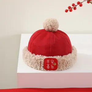 Detalle del gorro de invierno rojo para niño con bordado Ping'an Xile y pompones beige