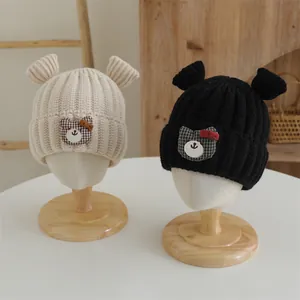 Détail de bonnets tricotés pour bébés avec oreilles d'ours et écusson ours à carreaux