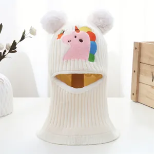 Close-up of knit baby balaclava with unicorn embroidery and fluffy white pom-poms
