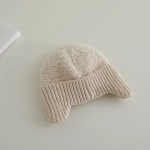 Details einer Wintermütze mit Ohrenklappen aus cremefarbenem Teddyvlies und Strick