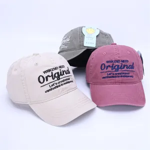 Close-up of three washed cotton baseball caps in beige, grey-green, and pink with embroidery