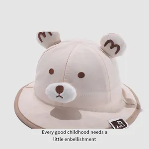 Detail of baby sun hat with cute bear ears and embroidered face features on beige fabric