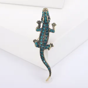 Vintage gold alloy crocodile brooch with sparkling teal rhinestones on a white background