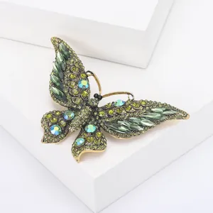 Macro-opname van vintage vlinderbroche met smaragdgroene kristallen op wit podium