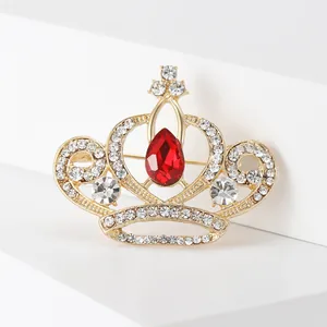Gros plan d'une broche couronne dorée avec cristal rouge et diamants scintillants