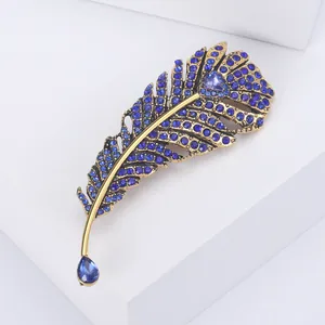 Elegant feather brooch with blue crystals and gold finish on a white stone pedestal