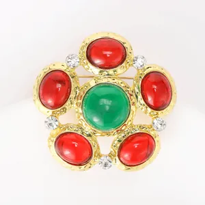 Detail of vintage flower brooch with green and red gemstones on gold hammered metal