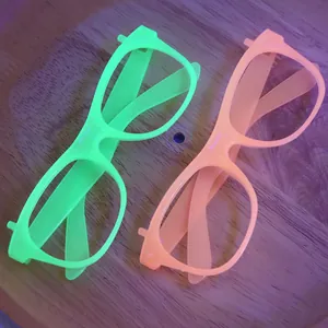 Neon green and orange party glasses frames glowing under UV light on wood tray