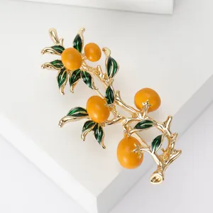 Detailed close-up of an orange branch brooch with golden texture and green enamel leaves