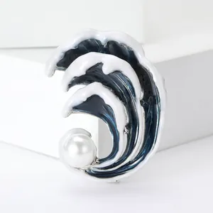 Macro detail of wave enamel brooch featuring a white pearl on a geometric stand