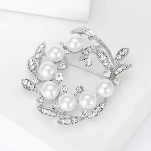 Détail d'une élégante broche couronne en perles avec feuilles argentées et strass
