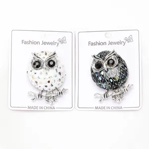 Close-up of owl brooches with abalone shell inlay and black gem eyes on white cards