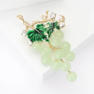Elegant gold grape brooch with green enamel leaves and translucent beads on white stand