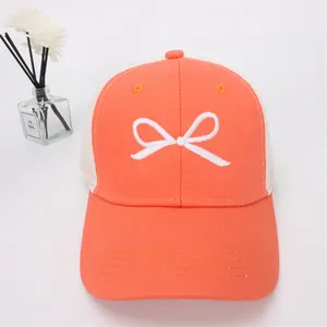 Detail of orange baseball cap featuring white bow embroidery and breathable mesh back