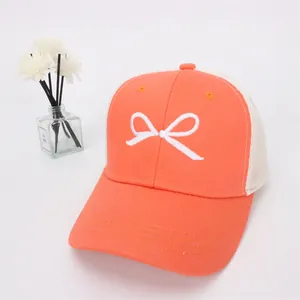 Detailed view of orange mesh baseball cap featuring white bow embroidery and breathable fabric