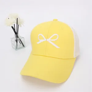 Detail of yellow mesh baseball cap featuring white bow embroidery and breathable design