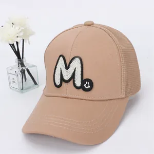 Detail of khaki mesh baseball cap with embroidered letter M and smiley face patch