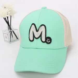 Detail of mint green mesh baseball cap with white towel embroidered M and smiley patch