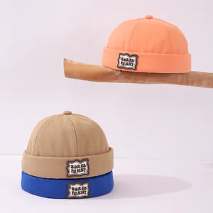 Detalle de gorros docker de algodón para niños en naranja, caqui y azul con parche de oso