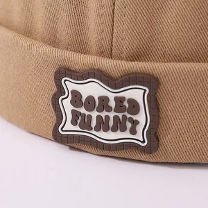 Detalle de gorro de algodón caqui con etiqueta de goma marrón y diseño de ondas blancas