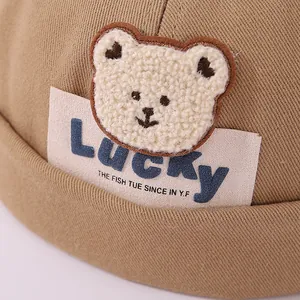 Detalle de gorro docker caqui con parche de oso de peluche y bordado Lucky azul