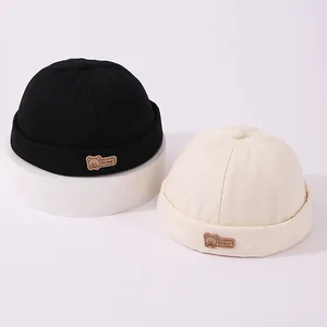 Detalle de gorros docker para bebé en negro y beige con parche de oso de cuero
