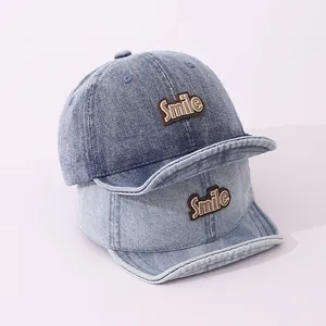 Detail view of two denim baby baseball caps with Smile patch on a soft purple background
