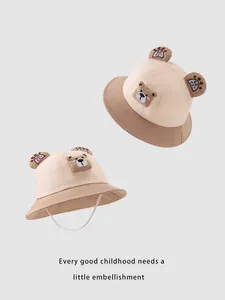 Détail de bobs pour enfants beige et marron avec oreilles d'ours et cordons coupe-vent