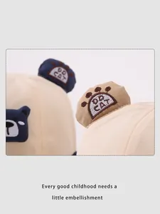 Détail d'un chapeau bob beige pour bébé avec broderie ours bleue et oreilles 3D