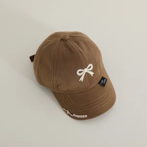 Close-up of brown cotton kids baseball cap with white 3D bow and edge embroidery