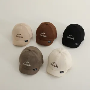 Flat lay of five corduroy baby baseball caps in neutral tones with mountain embroidery