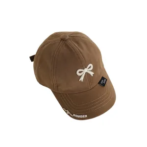 Brown kids cotton baseball cap with white bow and embroidered details on plain background