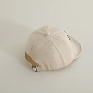 Detail of adjustable bronze metal buckle and cotton twill texture on beige baby baseball cap