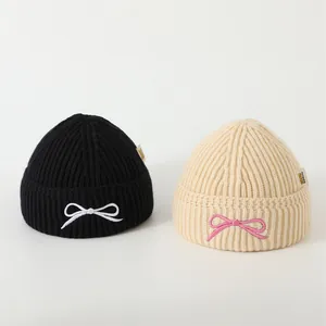 Detail of ribbed knit baby beanies featuring embroidered bows in black and beige colors
