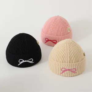 Three knitted winter beanies for kids with cute bow accents in black, pink, and beige