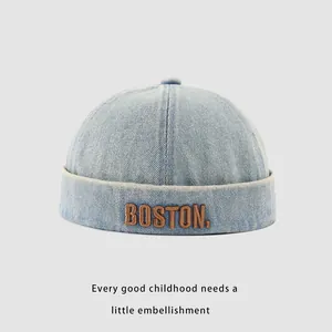 Detailed close-up of brown BOSTON embroidery on a light blue denim baby skullcap hat