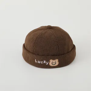 Detail of corduroy brimless docker hat with Lucky bear embroidery and stripe texture